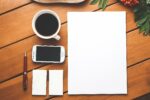 Image of blank business cards and paper on a wooden desk, next to coffee in a mug, a phone, and a pen.