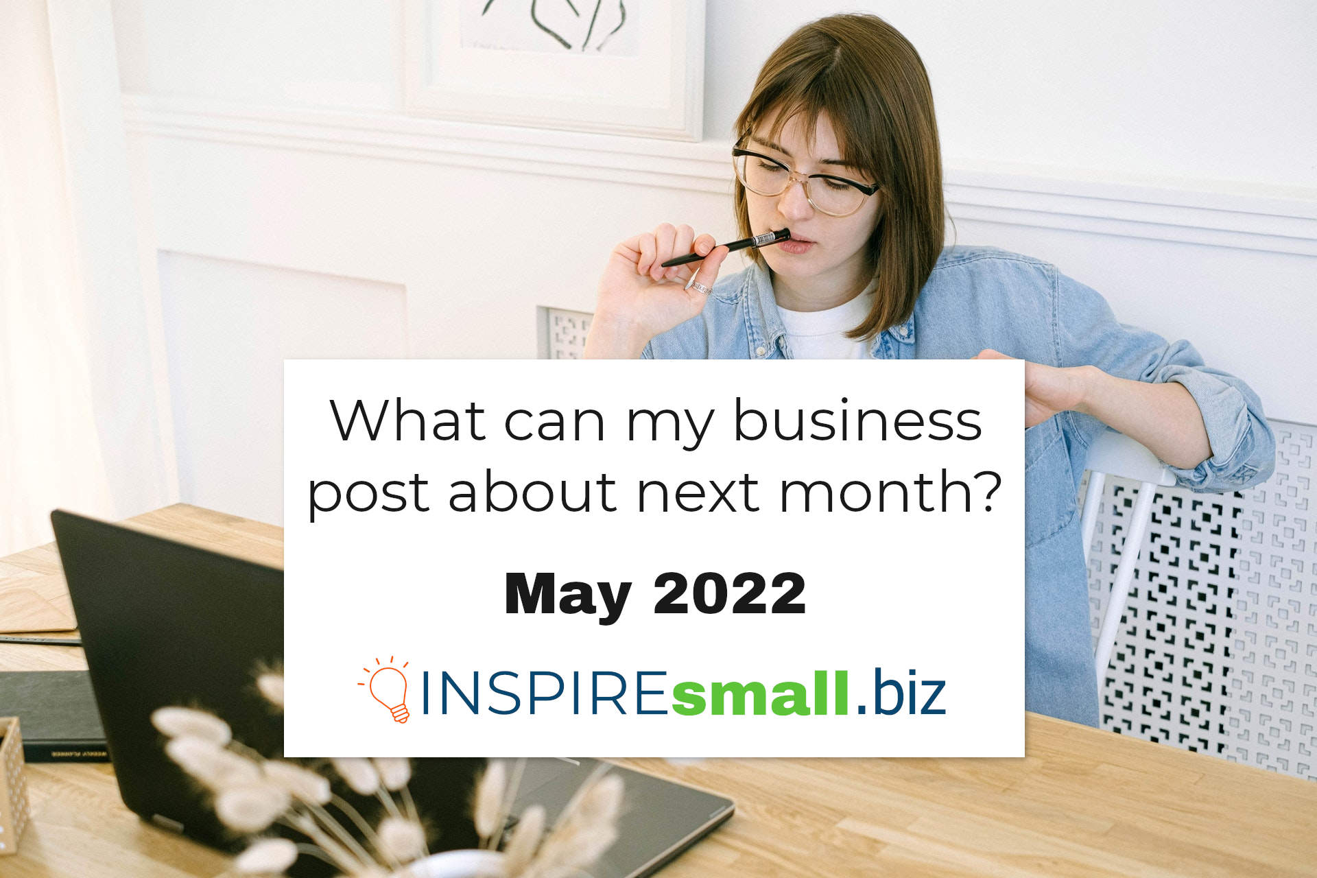 A woman sitting at her computer, chewing on her pen, thinking. With the text What can my business post about next month? May 2022, blog from INSPIREsmall.biz